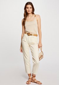 Beige tank top with textured straps, cream high-waisted pants, brown belt with a circular buckle, brown strappy sandals, small beige handbag.