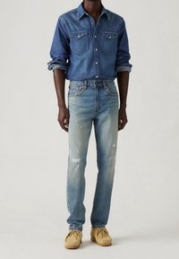 Denimová košile tmavě modré barvy s špičatým límcem, zapínacími kapsami a ohrnutými rukávy. Světle modré džíny s přímým střihem a jemným vyblednutím.