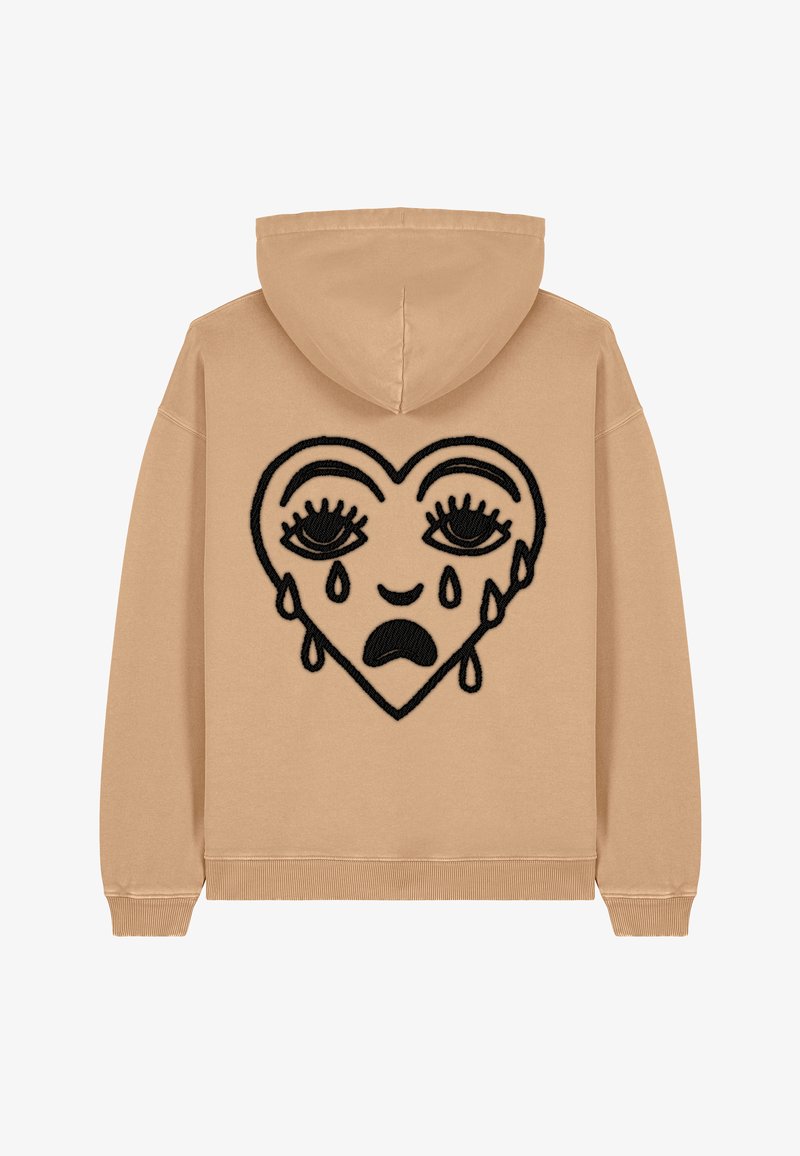 Haut à capuche beige mettant en avant un grand cœur noir brodé avec des yeux et des détails de larmes, fabriqué en tissu doux avec des poignets et un ourlet côtelés.