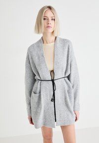 Szürke kardigán puha anyagból, laza szabású, nyitott elülső résszel, hosszú ujakkal, oldalsó zsebekkel és fekete kötővel.