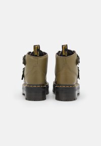 Botines de cuero verde con superficie texturizada, punta redonda y suela negra gruesa. Presentan costuras amarillas y correas con hebillas en los laterales.