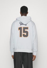 Persona que lleva una sudadera azul clara con "JOKIC" y el número "15" en letras grandes en la espalda, combinada con pantalones negros.