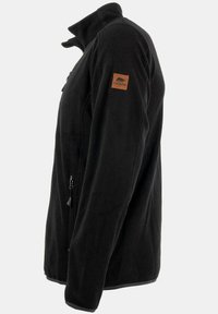 Giacca in pile nera con collo alto, chiusura con zip e tasche laterali. Presenta una toppa in pelle marrone con il logo sul braccio sinistro.