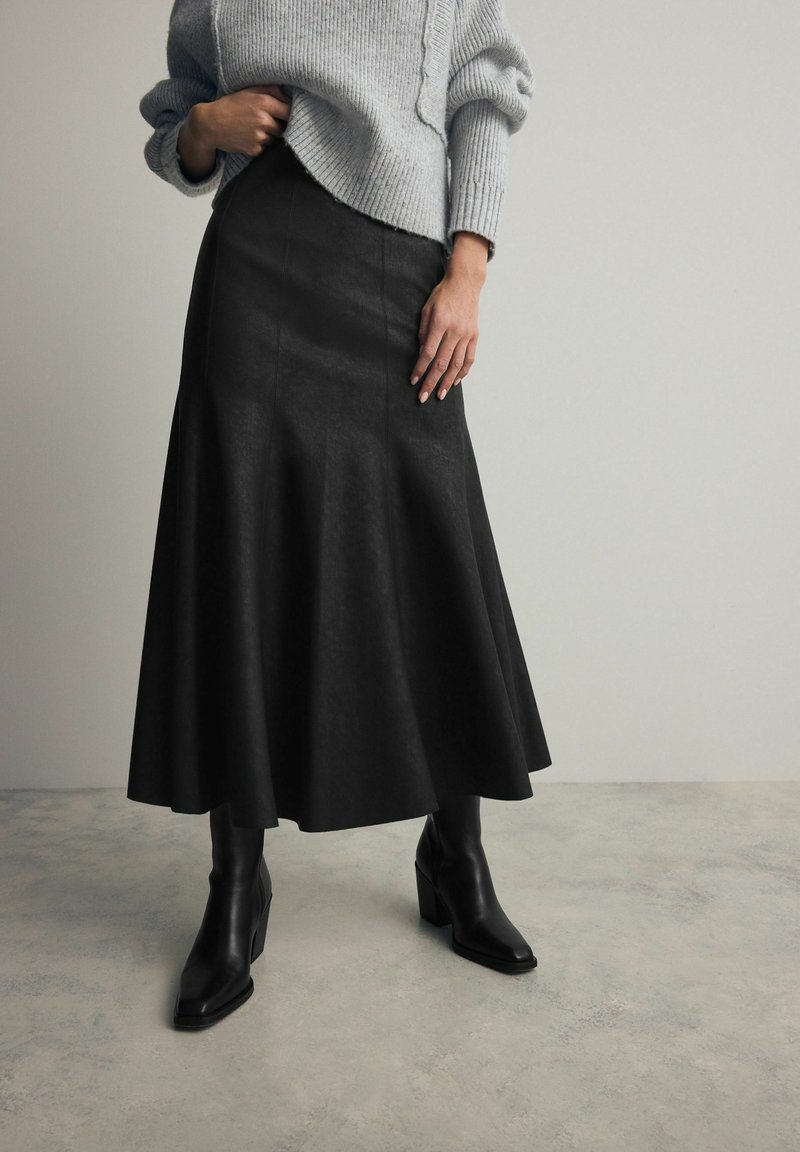 Svart läder maxi kjol med utsvängd nederdel, ihop med åtsittande svarta ankelboots. Outfitten kompletteras av en grå ribbad tröja.