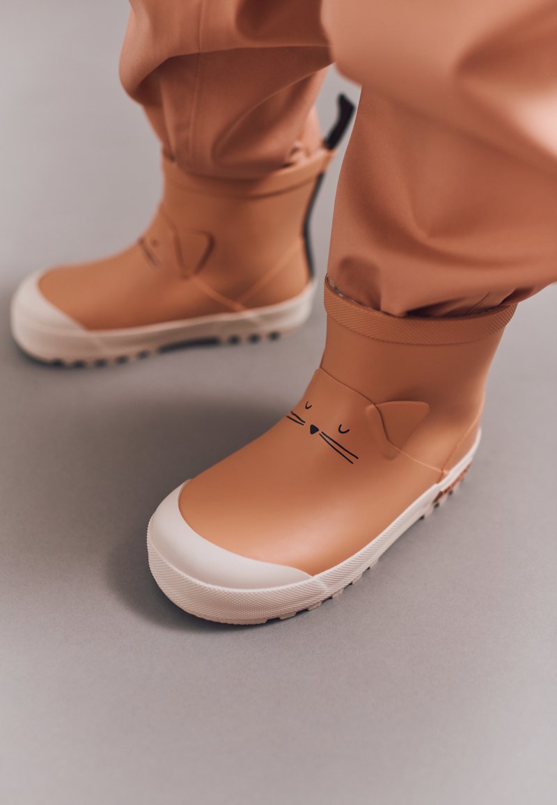 Bottes imperméables beiges avec des semelles blanches, présentant un design de visage de chat avec des oreilles et des moustaches. Texture lisse avec un ajustement flexible.