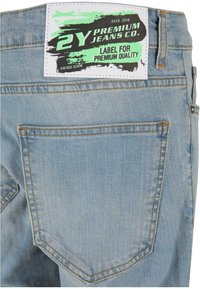 Vaaleansiniset farkut, joissa on suorakulmainen merkki takahihnassa, jossa on mustaa ja vihreää tekstiä 2Y Premium Jeans Co.