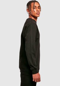 Felpa nera a maniche lunghe in cotone. Presenta un colletto a girocollo, polsini a coste, vestibilità rilassata e un design minimalista senza motivi.