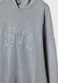 Felpa grigia con tasca frontale, con la scritta "LOVE" in carattere consumato. Realizzata in tessuto morbido, ha una vestibilità comoda e cappuccio regolabile.