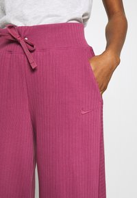 Pink ribbed joggers featuring a drawstring waist and side pockets. Nike logo embroidered on the left side. Soft fabric texture.