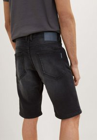 Shorts en denim noir à coupe slim, dotés de poches arrière et d'une texture légèrement délavée. Agrémentés d'un patch en cuir griffé à la taille.