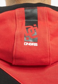 Red and black hoodie with a textured finish; features a prominent black label with white "DNGRS" branding on the back.