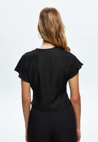 Černý krátký rukáv top s volným střihem, kulatým výstřihem a měkkou, lehkou tkaninou. Hladká textura, minimalní designové detaily.