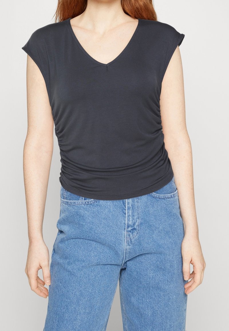 Top gris foncé à col en V avec des manches courtes et des détails froncés sur les côtés, associé à un jean taille haute bleu clair. Texture lisse.