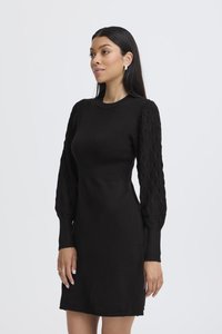 Abito nero in maglia con corpetto a coste e maniche gonfie e strutturate. Presenta una scollatura rotonda e una silhouette aderente sopra il ginocchio.