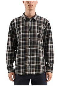 Camicia di flanella a quadri bianca e nera con accenti marroni, maniche lunghe e chiusura frontale a bottoni. Presenta un colletto classico e una tasca sul petto.