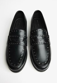 Fekete bőr mokaszin fényes felülettel, díszítő ezüst szegecsekkel a tetején, klasszikus kerek orrész dizájnnal.