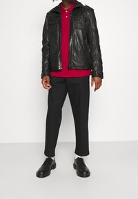 Zwarte leren jas met ritsen en zakken, rood poloshirt, zwarte cropped broek en zwarte schoenen met witte sokken. Eenvoudig, modern ontwerp.