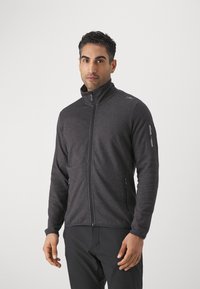 Veste zippée gris foncé en tissu texturé. Elle présente un col haut, des poches latérales et une poche zippée sur la manche.