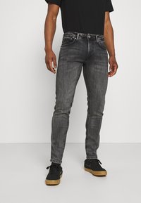 Slim-fit černé džíny vyrobené z denimu s jemnýma zabarvením, pěti kapsami a decentními švy. Nahoře obuté s černými teniskami.