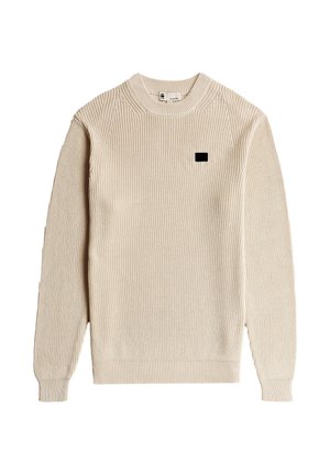 Beige geribbelde trui met een ronde hals, lange mouwen en een klein zwart logoplaatje op de borst. Getextureerde stof met een nauwsluitende pasvorm.