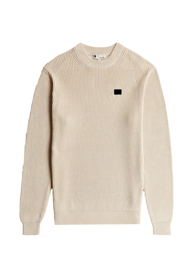 Jersey beige acanalado con cuello redondo, mangas largas y un pequeño parche negro con logo en el pecho. Tejido texturizado con un ajuste ceñido.