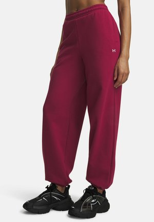 Vrouw draagt loszittende magenta joggingbroek met hoge taille, elastische boorden en zwarte sportschoenen, staand op een effen witte achtergrond.