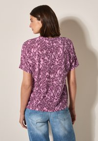 T-shirt à manches courtes dans des nuances de rose et de violet avec un motif texturé et abstrait. Coupe décontractée avec un col rond et des manches amples.