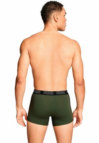 Boxer shorts verde oscuro con una cinturilla negra que presenta el logo de 'PUMA', vistos desde la parte trasera en un modelo con cabello rizado corto.