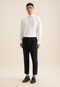 Camicia a quadri bianca con bottoni e maniche lunghe, abbinata a pantaloni su misura blu navy e scarpe in pelle nera. Design semplice e classico.