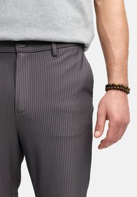 Grå stribede bukser lavet af glat stof, med knaplukning, sidelommer og en tætsiddende design langs taljen og hoften.