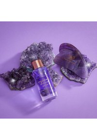 Flacon en verre violet avec un bouchon doré, étiqueté "Sérum Scintillant Cristallisé." Entouré de cristaux d'améthyste et d'une pierre gua sha violette.