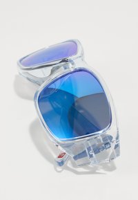 Transparente Sonnenbrille mit lila-blauem Farbverlauf, eckiger Form, dicken Rahmen und kleinem roten Logo-Detail an der Seite.