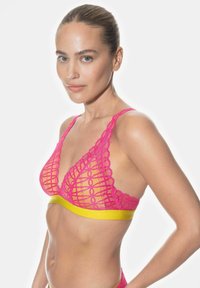 Bralette de encaje en un pink vibrante con una banda amarilla, con diseño geométrico, forma en V profunda y bordes ondulados.