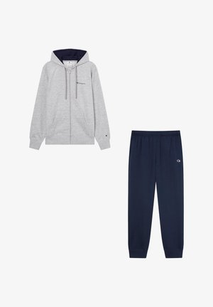Felpa grigia con zip e fodera interna navy, abbinata a pantaloni della tuta navy con vita elastica e dettaglio del logo.