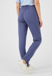 Blaue Baumwoll-Jogginghosen mit elastischem Bund. Schmal zulaufendes Design und Bündchen; glatte Textur. Kombiniert mit weißen Turnschuhen.