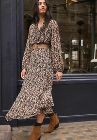 Beige, brun och svart klänning med blommönster och långa ärmar, med en volang nederkant. Kombinerad med ett flätat läderskärp och bruna ankelstövlar.