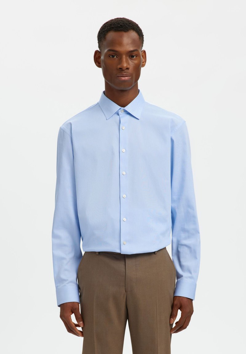 Ανοιχτό μπλε πουκάμισο με κουμπιά, γιακά τύπου spread και μακριά μανίκια, με λεπτό ριγωτό σχέδιο, συνδυασμένο με καφέ παντελόνι κανονικής ραφής.
