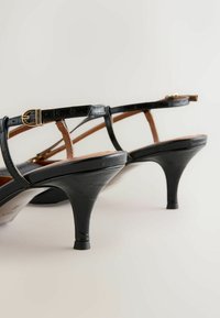 Mustad lakknahast kontsakingad, õhukeste rihmade ja kuldsete pandlatega, tekstuurse pinnaga. Avatud kannaosa disain.