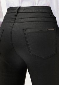 Jeans negros de corte ajustado, cintura alta, costuras sutiles y dos bolsillos traseros. Tejido suave con un ligero brillo, detalles de herrajes mínimos.