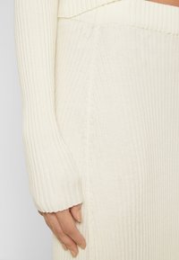 Ribbad vit tröja med hög krage och långa ärmar. Den har en figurnära passform och en mjuk, texturerad finish som framhäver tyget.