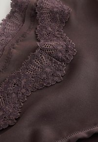 Tumepruuni kangas keeruka lillelise pitsäärega, mis on õmmeldud mööda õmblust, näidates peenikest õmblemist ja õrna tekstuuri detaile.