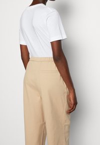 Vit kortärmad T-shirt i kombination med beige byxor med elastisk midja, som har sidfickor och en bakficka.