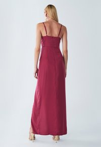 Maxikleid aus tiefburgunderfarbenem Satin, mit dünnen verstellbaren Trägern, einem taillierten Oberteil und einem fließenden Rock mit seitlichen Schlitzen.