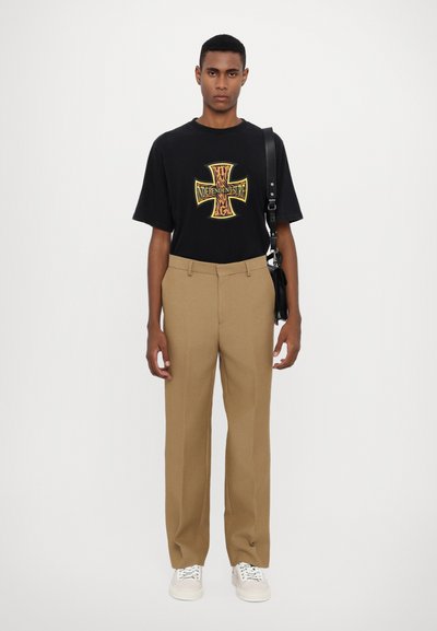 T-shirt nera con un design grafico colorato che presenta una croce, abbinata a pantaloni beige a vita alta e sneaker bianche.