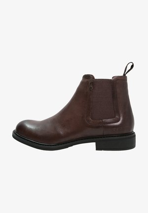Botte Chelsea en cuir marron avec panneaux latéraux élastiques, bout arrondi, languette de traction et semelle noire. Texture lisse avec des accents minimalistes.