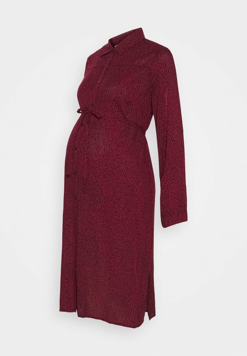 Umstandskleid in Burgunderrot mit einem dezenten schwarzen Punktmuster. Es verfügt über einen Kragen, lange Ärmel, einen Taillengürtel und seitliche Schlitze.