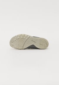 Suela de zapatilla gris con una superficie de goma texturizada. Presenta un patrón de tracción en forma de diamante para un mejor agarre y una ligera curvatura en el talón. Logo de marca notable visible.