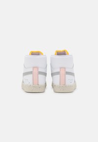 Höga sneakers med en vit syntetisk ovandel, grå detaljer, en rosa hällapp och en texturerad beige sula med en logotyp.