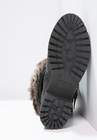 Černá bota s texturovanou gumovou podrážkou se vzorem srdcí a pikových symbolů, doplněná kožichem podél horního okraje.