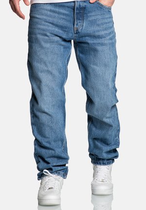 Hellblaue Denim-Jeans mit einer lockeren Passform, die über Nähte, fünf Taschen und Hosenbeine verfügen, die über weißen Sneakern enden.